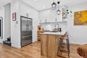 Una cocina moderna con refrigerador de acero inoxidable, armarios de madera y una isla central con taburetes.