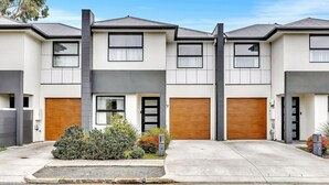A modern two-story residential building with a garage, a front door, and a small garden area. - The Art House | Courtyard + Alfresco Living (Campbelltown)