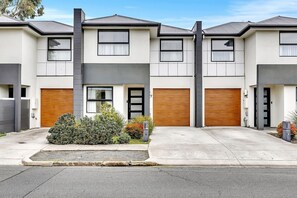 A modern two-story residential building with a garage, a front door, and a small garden area. - The Art House | Courtyard + Alfresco Living (Campbelltown)