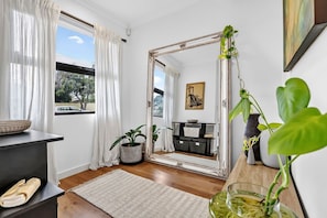 Une pièce avec un grand miroir, une plante en pot, un tapis et une fenêtre avec des rideaux.