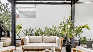 A modern outdoor seating area with a sofa, wooden chairs, and a round table. - The Art House | Courtyard + Alfresco Living (Campbelltown)