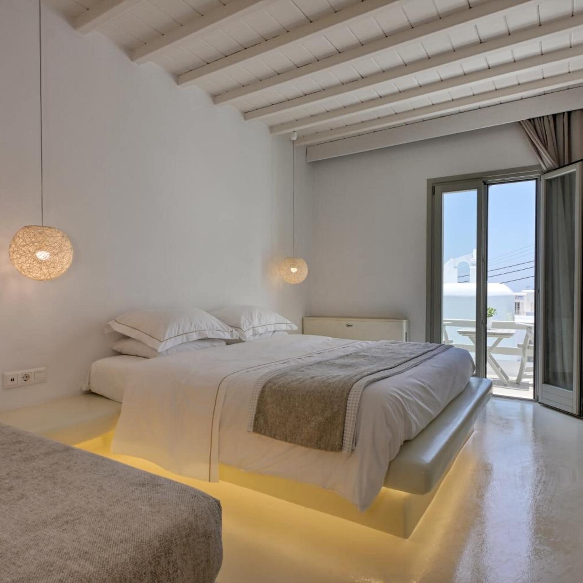Une chambre à coucher moderne, avec un lit, une table de chevet et une vue sur la mer par une grande fenêtre.