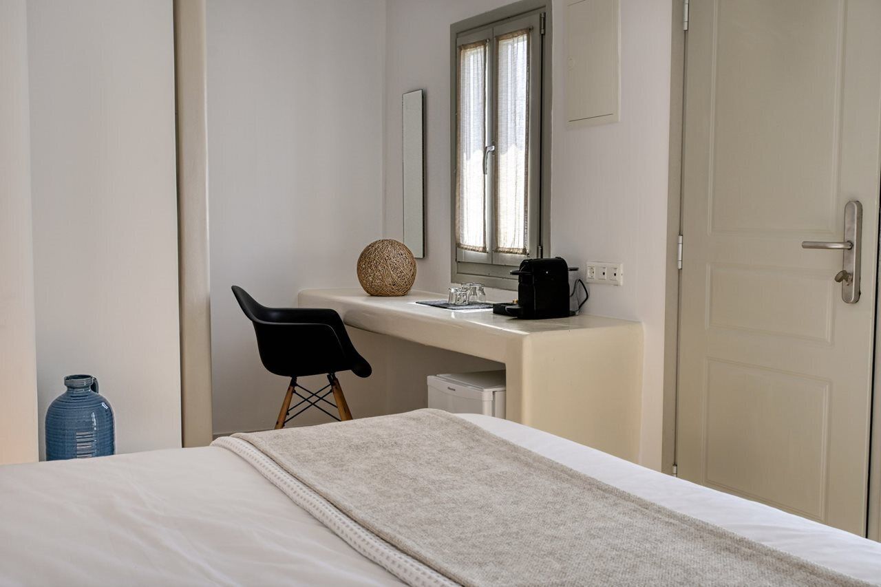 A hotel room with a bed, a desk with a chair, a window, and a door.
