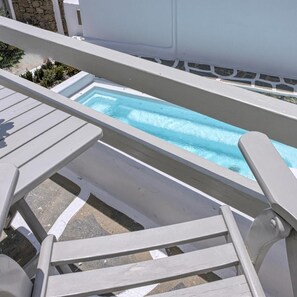 Ett poolområde med en bubbelpool, vita solstolar och en stenmur i bakgrunden.