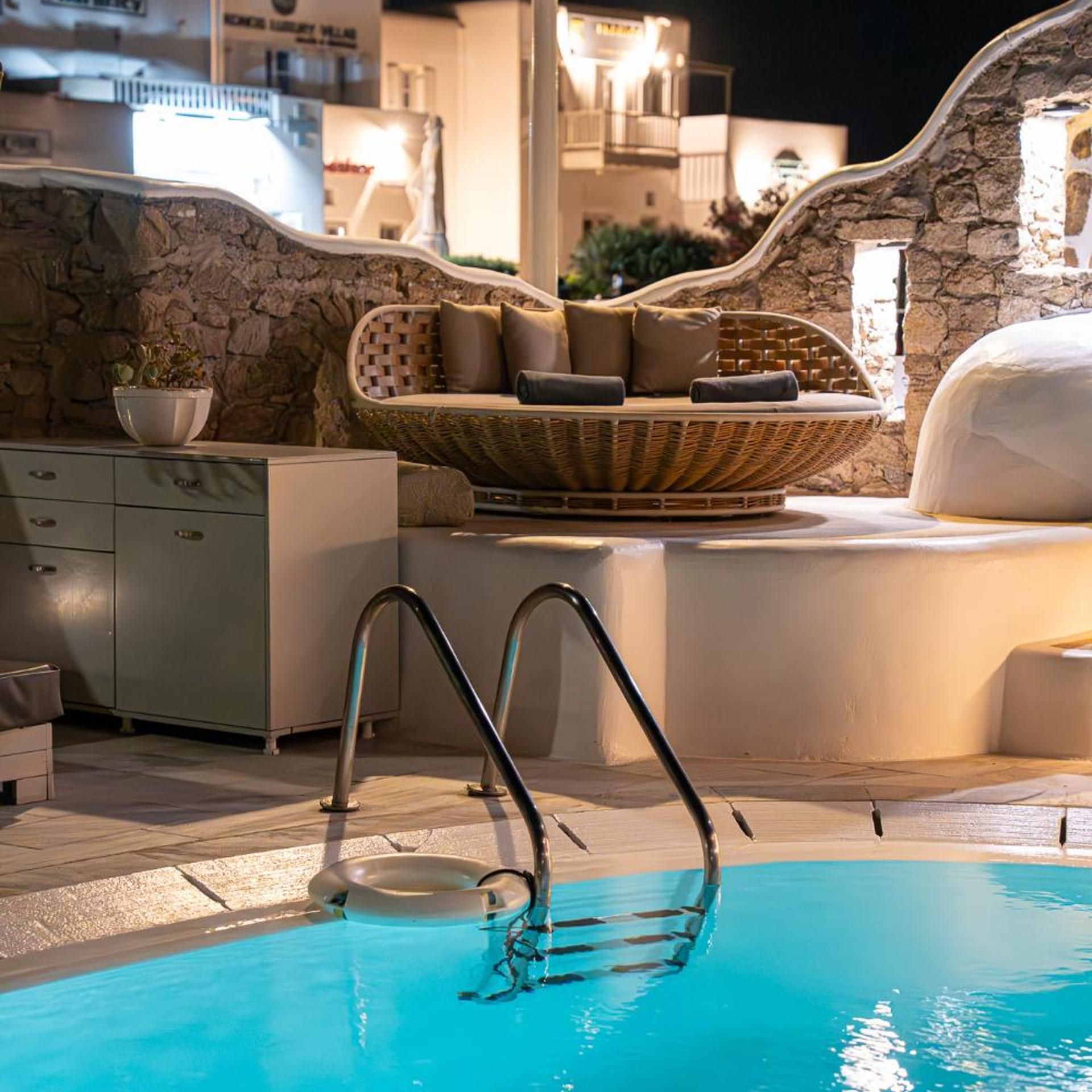 A pool area with a stone wall, a wicker sofa with cushions, a white cabinet, and a metal ladder leading into the pool.