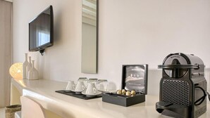 Camera d'albergo con un bancone bianco, una macchina da caffè Nespresso, un set di capsule Nespresso incorniciato e tazze di ceramica bianca.