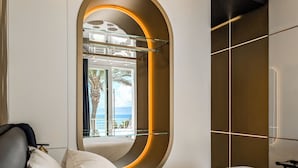 A modern hotel room with a curved mirror, a bed with white linens, and a view of the ocean through large windows. - Hotel Nautilus Excelsior - Adults Only (Cagliari)