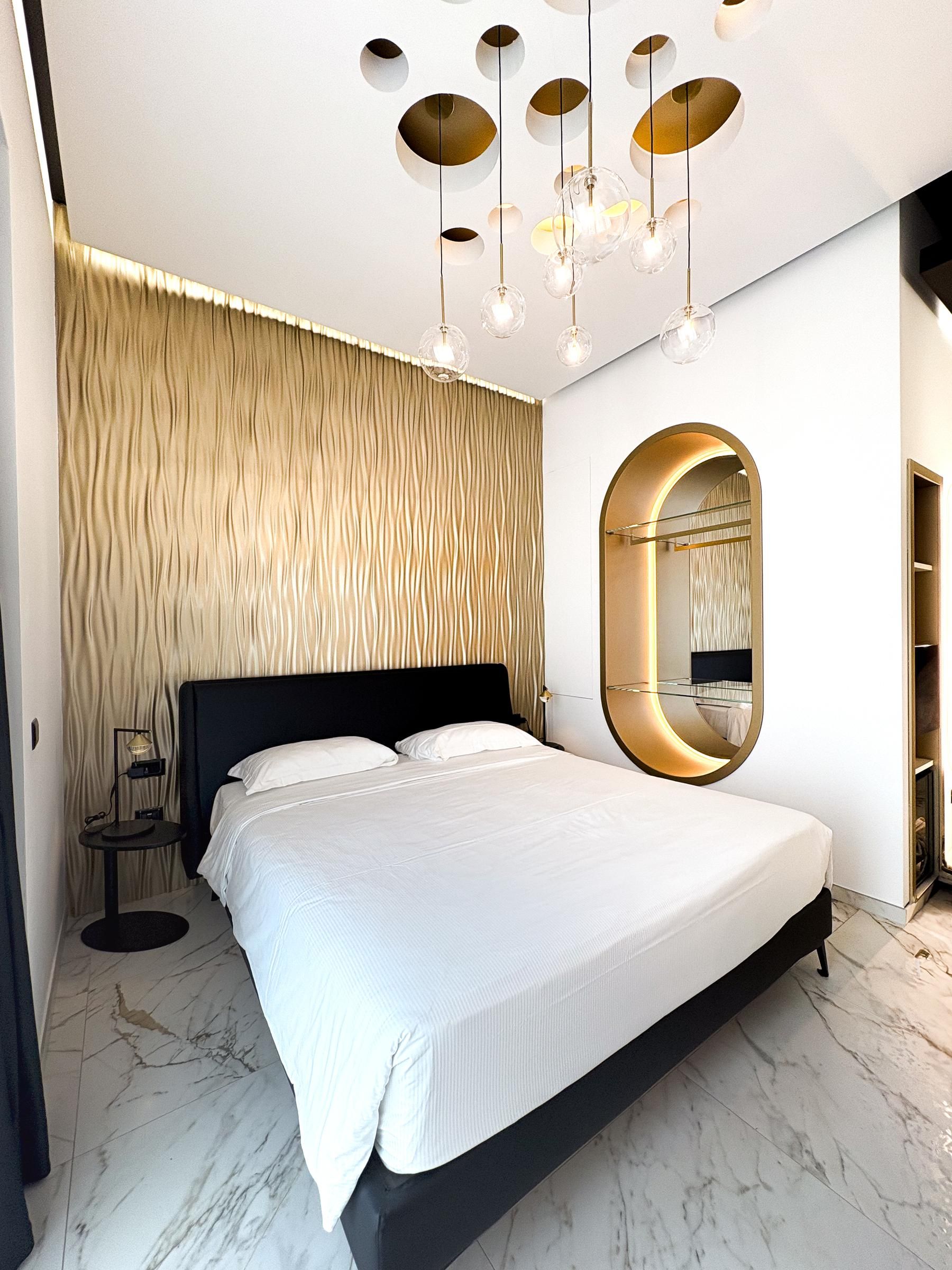 A modern bedroom with a large bed, a round mirror, and a unique ceiling light fixture.