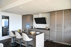 A modern kitchen with a central island, bar stools, a built-in oven, and a flat-screen TV. - Luxury Corba Lake View Apartment With Terrace (Canobbio)