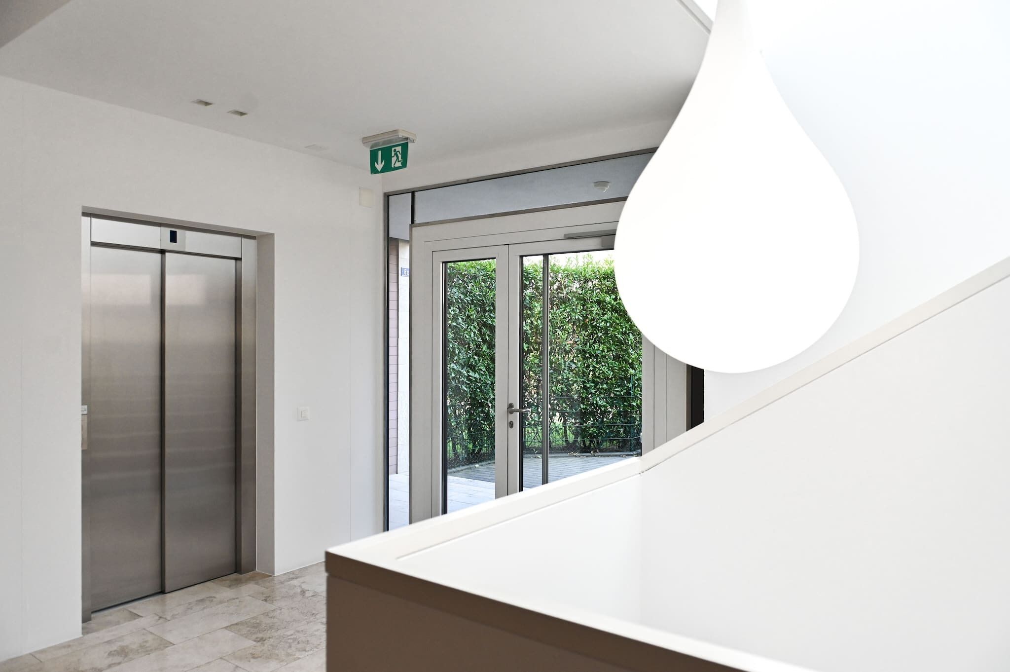 A modern interior with a staircase, an elevator, and a large window with a view of greenery.