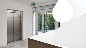 Um interior moderno com escada, elevador e uma janela ampla com vista para o verde.