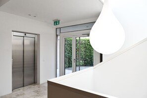 Ein modernes Interieur mit Treppe, Aufzug und einem großen Fenster mit Blick ins Grüne.
