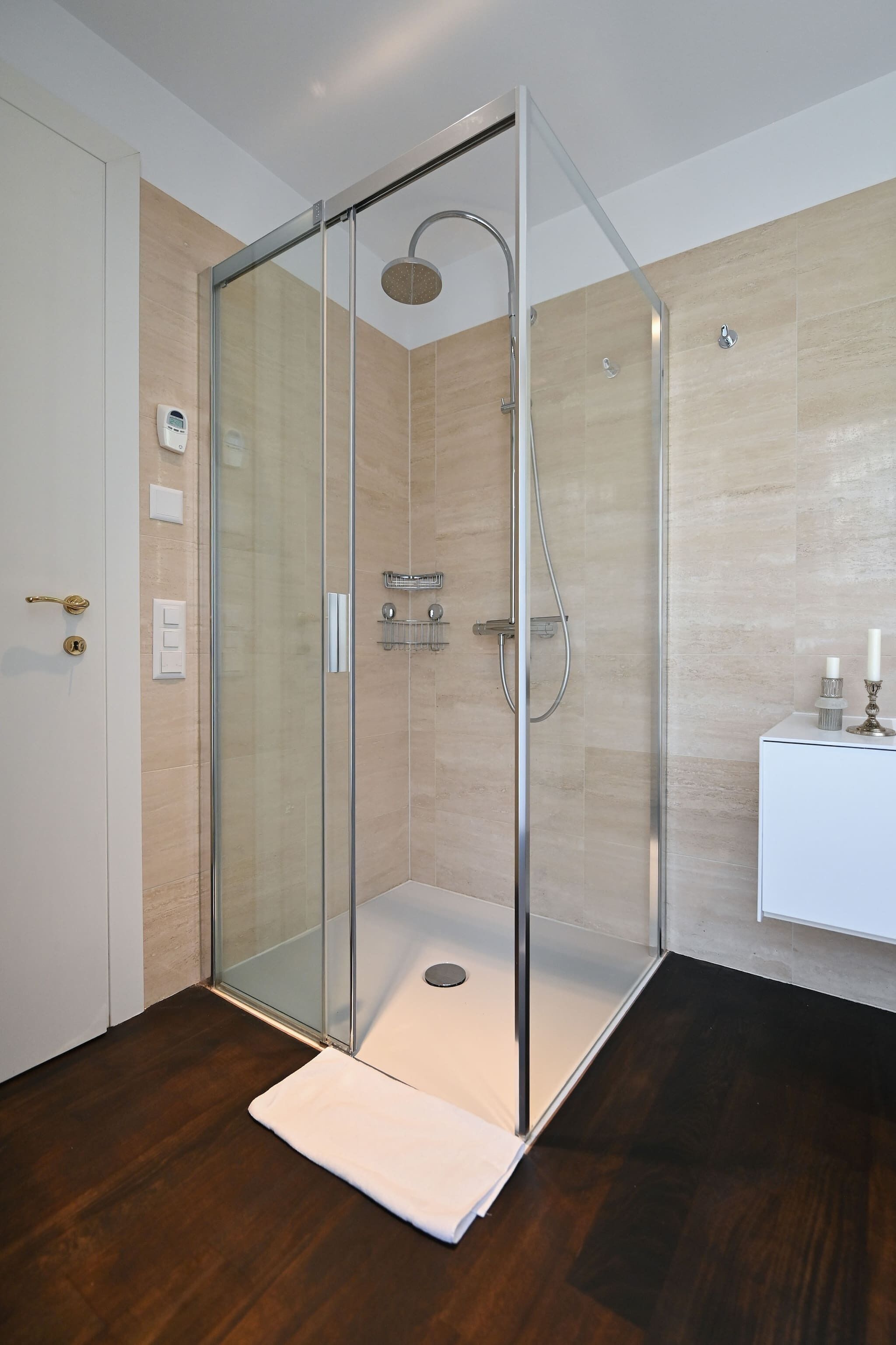 A modern bathroom with a glass-enclosed shower, a white sink, and a wooden floor.