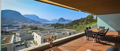 A modern outdoor terrace with a dining area, a potted plant, and a view of a cityscape and mountains.