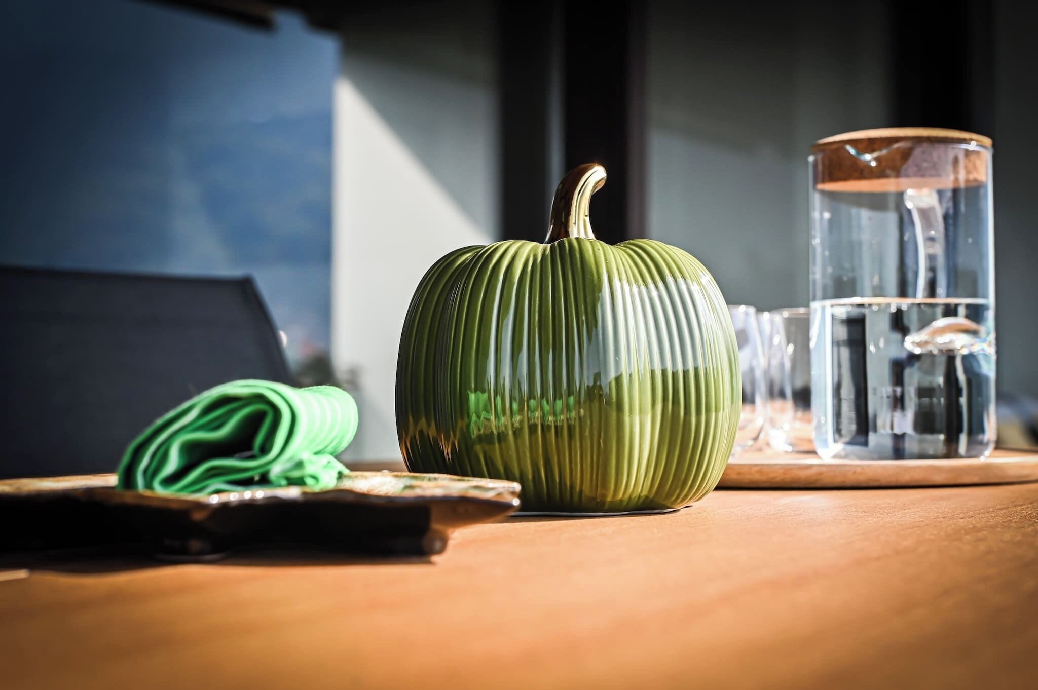 Une table en bois avec une citrouille verte, un verre d’eau et un ordinateur portable.