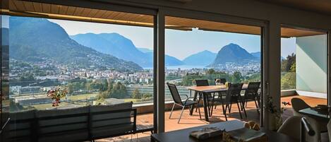 Un balcón con un banco de madera, una mesa con sillas y vistas a la ciudad y montañas.