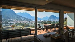 Un balcón con un banco de madera, una mesa con sillas y vistas a la ciudad y montañas.