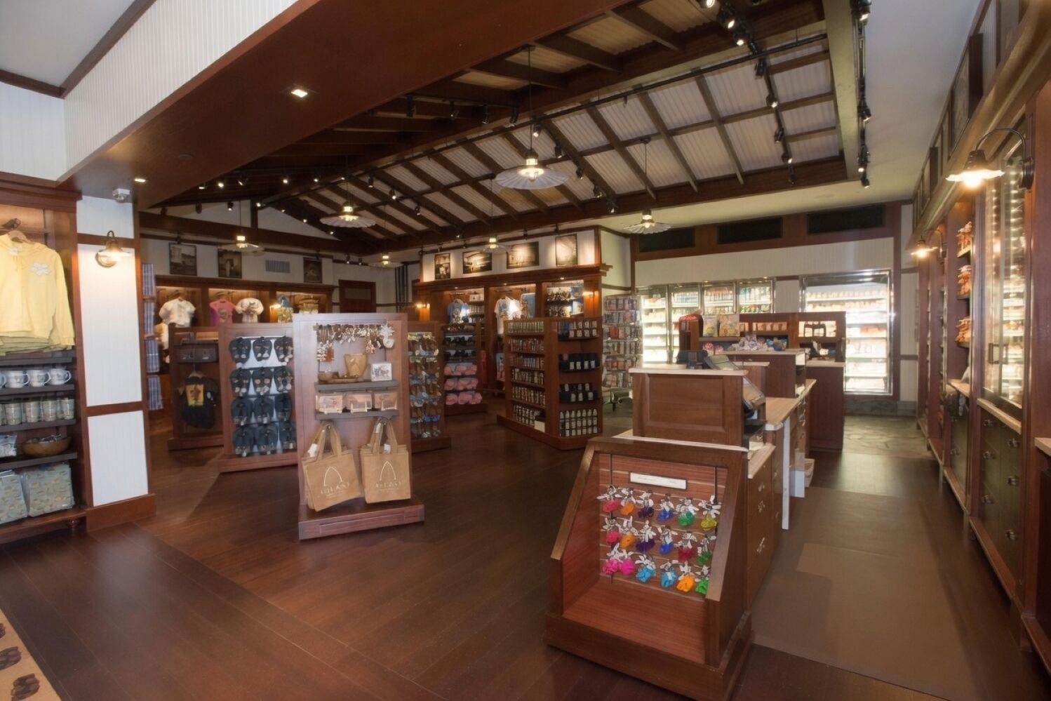 A spacious retail store with wooden flooring and high ceilings, featuring various merchandise displays and a refrigerated section.