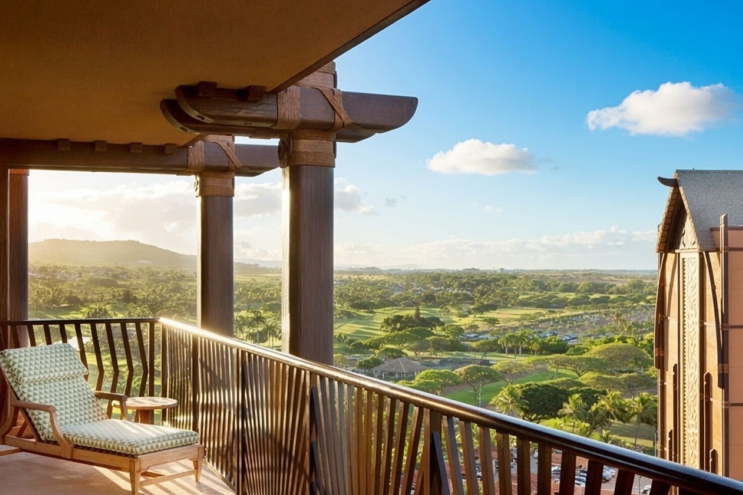Ein Balkon mit Blick auf eine grüne Landschaft, ein Holzstuhl und ein Gebäude mit einer Stein-Fassade.