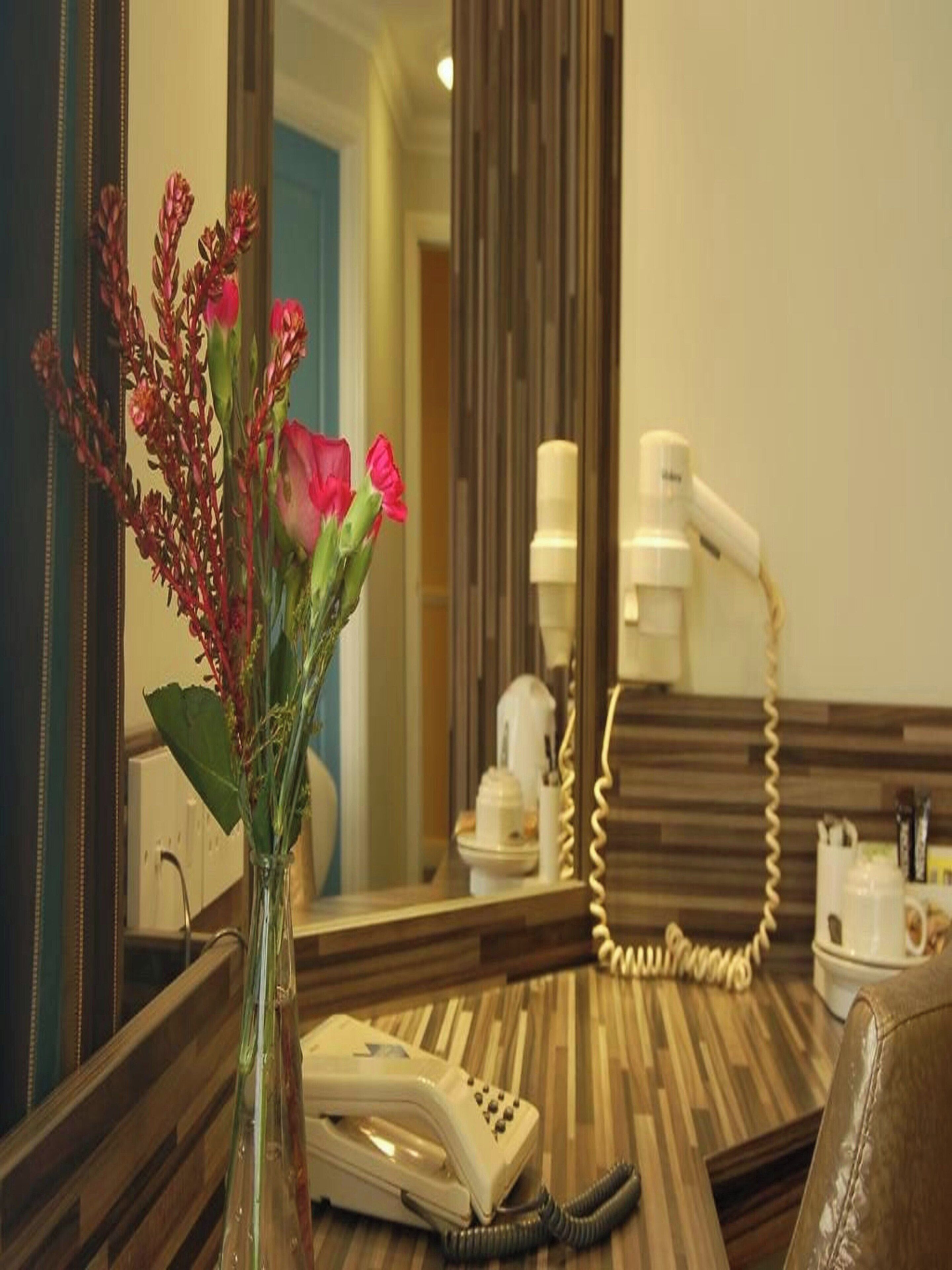 Une chambre d’hôtel avec une coiffeuse en bois, un téléphone, un vase de fleurs et un miroir qui reflète la pièce.