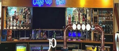 Zona de bar con un letrero de neón que dice 'Cafe Bar', una barra con el número '20' encima, y una variedad de botellas y vasos en estantes.