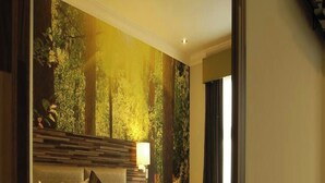 A hotel room with a large bed, a bedside table, a lamp, and a view of a forest through the window.