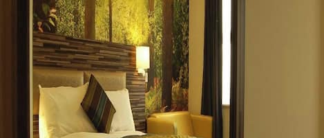 A hotel room with a large bed, a bedside table, a lamp, and a view of a forest through the window.