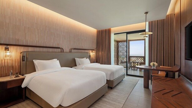 A hotel room with two beds, a desk, a TV, and a balcony with a view.
