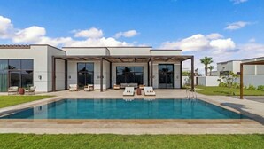 Une maison moderne dotée d’une piscine, d’un espace salon extérieur et d’un patio couvert.