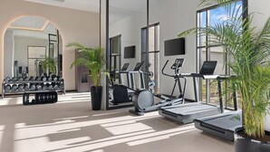Une salle de sport moderne équipée de matériel d’exercice, notamment des tapis de course et un rameur, ainsi qu’un porte-haltères.