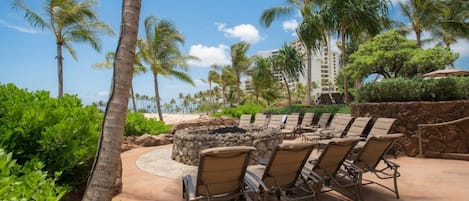 A resort with a pool area, lounge chairs, palm trees, and a view of the beach.