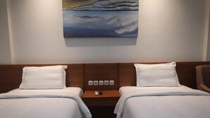A hotel room with two beds, a painting on the wall, and a nightstand with a phone and a remote control. - Gemma Hotel Balige (Balige)