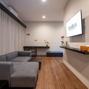 A modern living room with a grey sectional sofa, a small table, and a mounted screen displaying 'Aralea Co Living'. - Aralea Co Living (Denpasar)