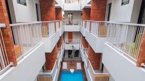 A multi-level indoor swimming pool with a central water feature, surrounded by balconies with white railings and brick accents.