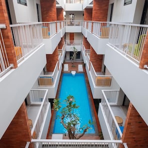 A multi-level indoor swimming pool with a central water feature, surrounded by balconies with white railings and brick accents.