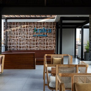 A reception area with a wooden reception desk, wicker chairs, and a wall with a geometric pattern. - Aralea Co Living (Denpasar)