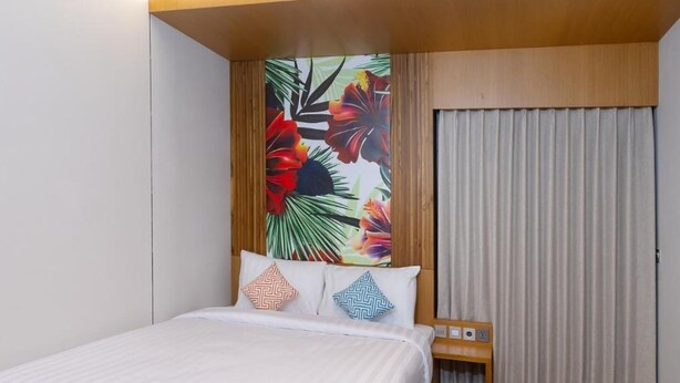 A hotel room with a bed, a nightstand, a wall with a tropical mural, and a window with curtains.
