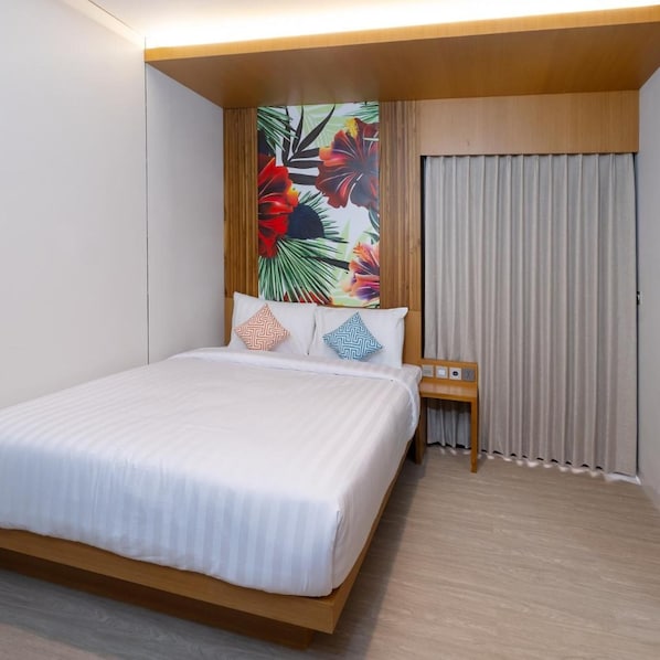 A hotel room with a bed, a nightstand, a wall with a tropical mural, and a window with curtains.