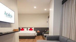 A modern hotel room with a bed, a sofa, a small table, and a TV mounted on the wall.