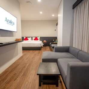A modern hotel room with a bed, a sofa, a small table, and a TV mounted on the wall.