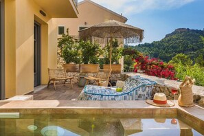 An outdoor pool area with lounge chairs, a table, and a decorative umbrella. - Chromata Assos Villas Kefalonia (Kefalonia)