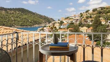 A balcony with a view of a coastal town, a table with a vase and books, and a chair.