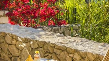 An outdoor seating area with a stone wall, a table with food and drink, and a wicker chair.