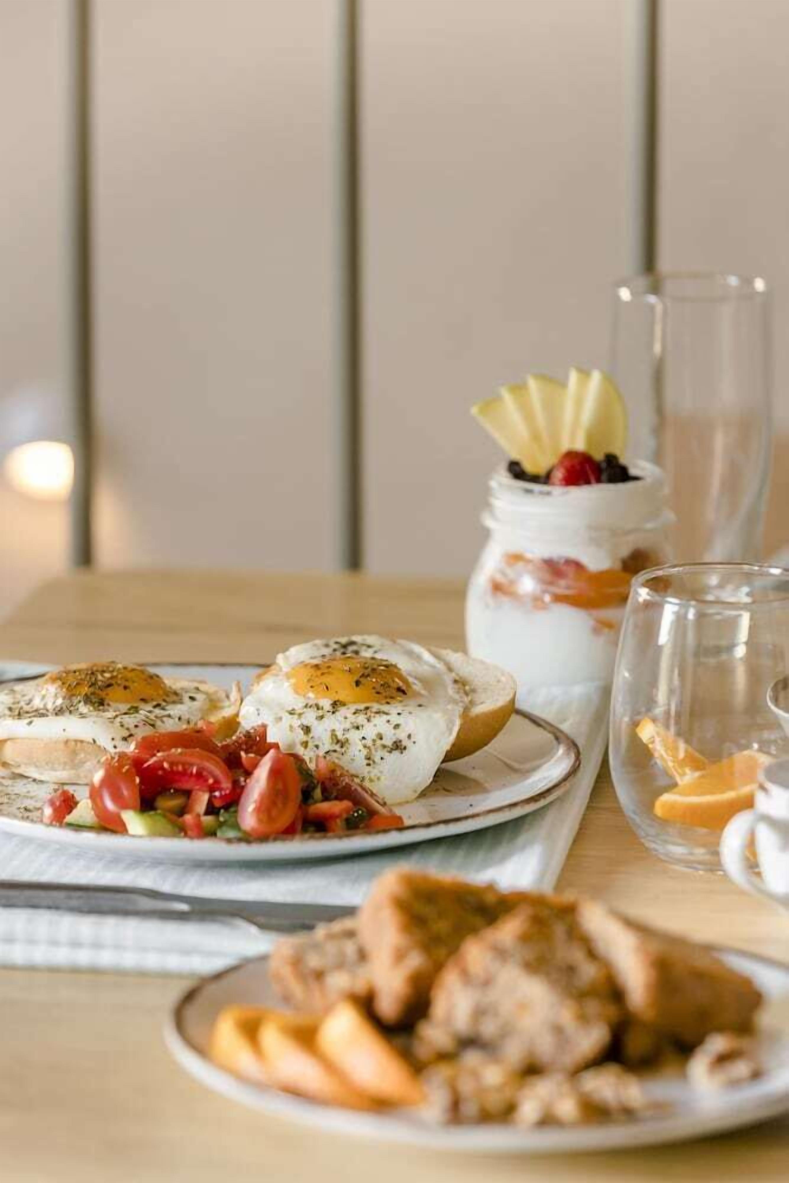 A breakfast setting with eggs, tomatoes, and a dessert in a jar.