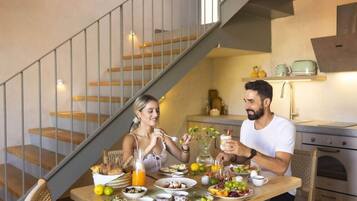 Un coin repas avec une table en bois dressée pour deux personnes, un escalier et une cuisine en arrière-plan.
