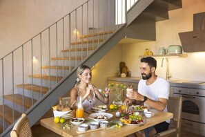 Un comedor con una mesa de madera preparada para dos personas, una escalera y una cocina al fondo.