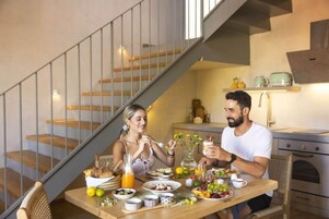 Un comedor con una mesa de madera preparada para dos personas, una escalera y una cocina al fondo.