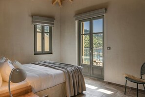 Un dormitorio con cama, una silla, una lámpara y un amplio ventanal con vista a la vegetación.