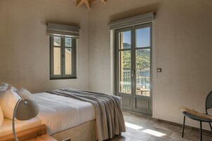 Un dormitorio con cama, una silla, una lámpara y un amplio ventanal con vista a la vegetación.