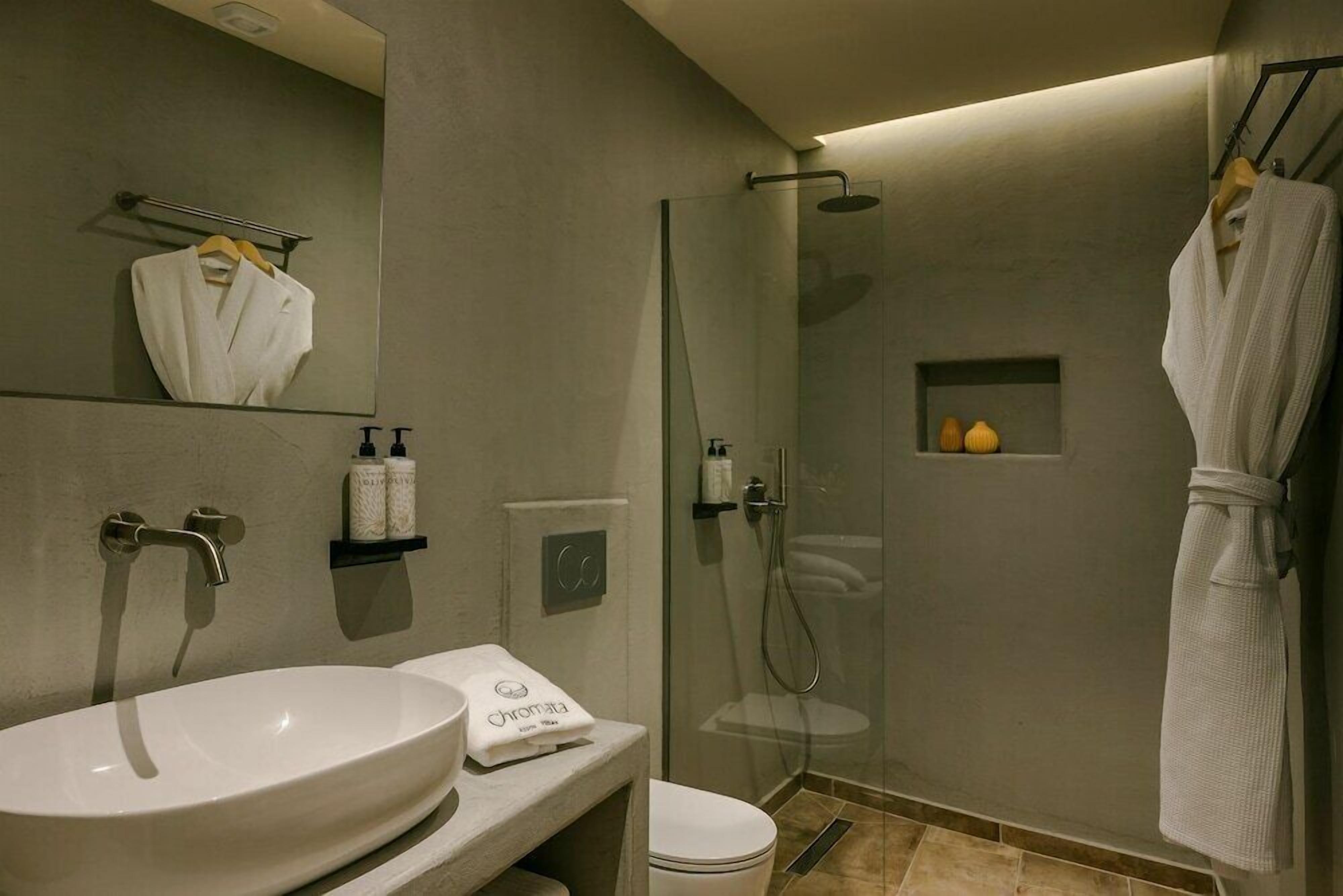 Ein modernes Badezimmer mit einem großen Spiegel, einem Waschbecken, einer Dusche und einem Bademantel, der auf einem Haken hängt.